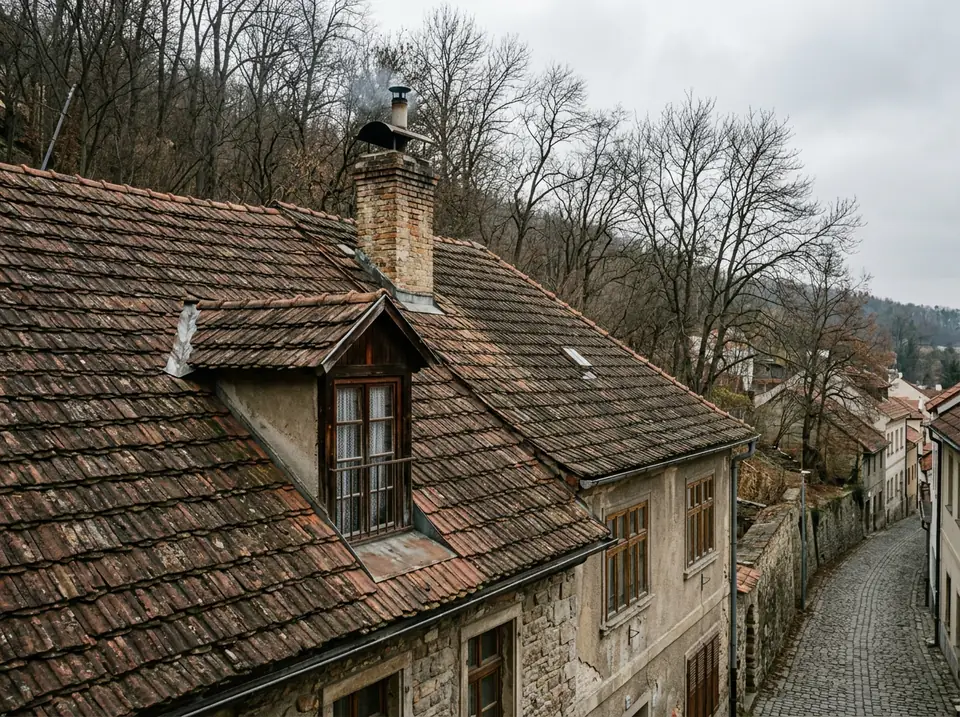 Cserépfedésű nyeregtető egy domboldali régi lakóház tetején, ősz fák a háttérben